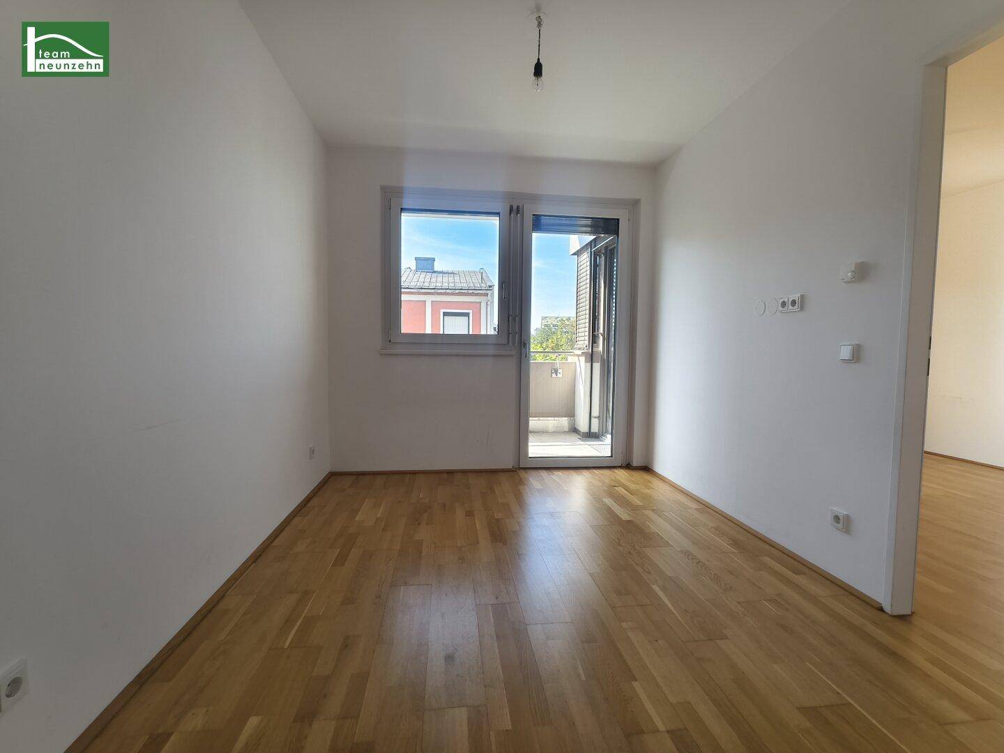 Heller Raum mit Holzboden und Zugang zu einem Balkon, geeignet als Wohn- oder Schlafzimmer.