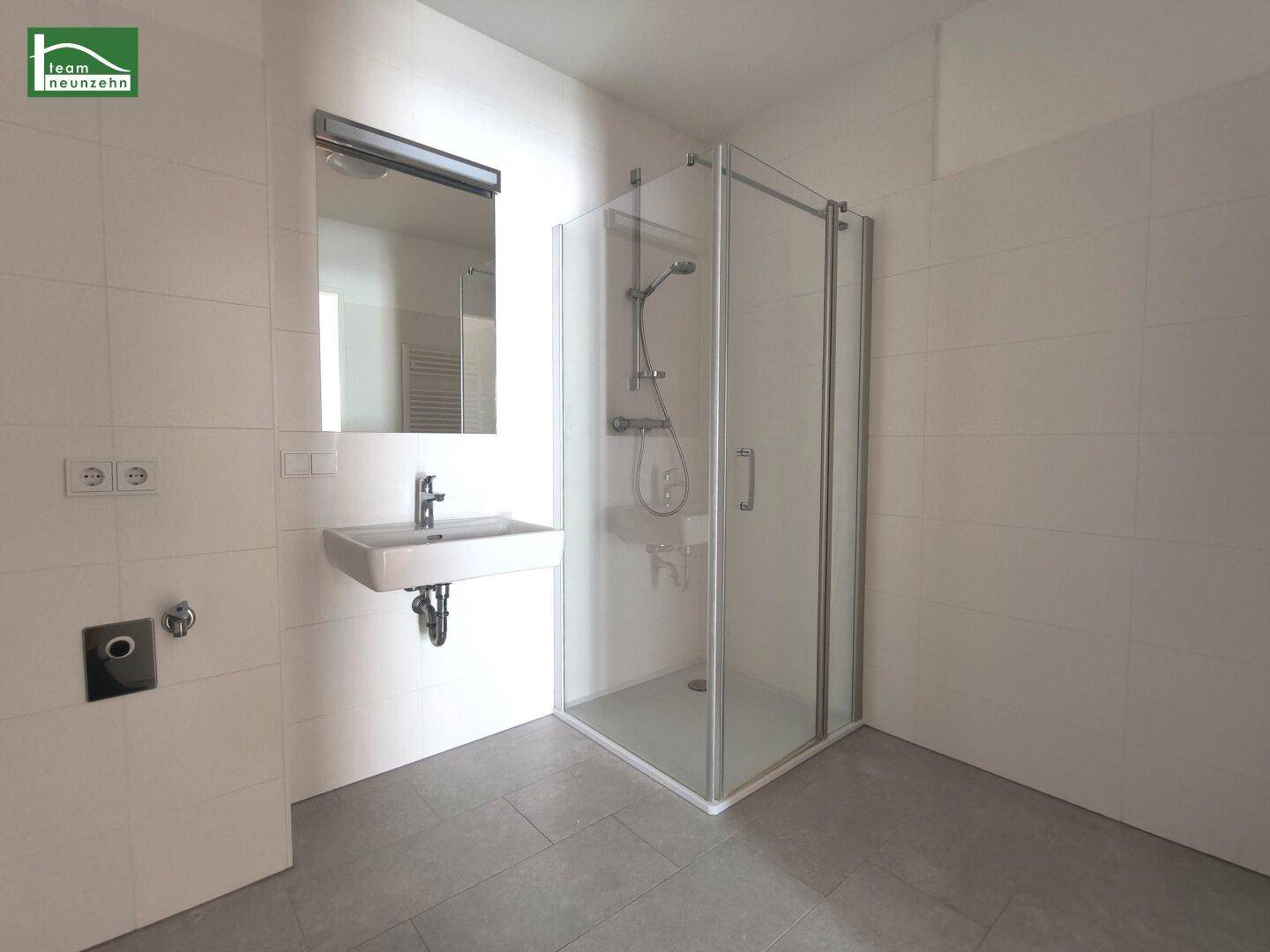 Modernes Badezimmer mit weiß gefliesten Wänden, Waschbecken und einer Glasduschkabine.