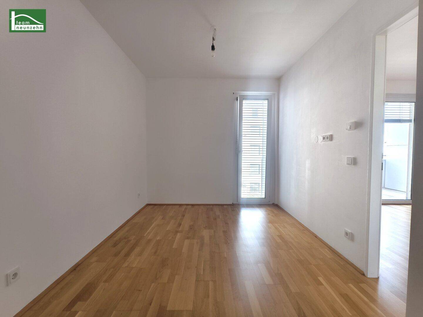 Heller Raum mit Parkettboden und einer Balkontür, die viel Tageslicht hereinlässt.