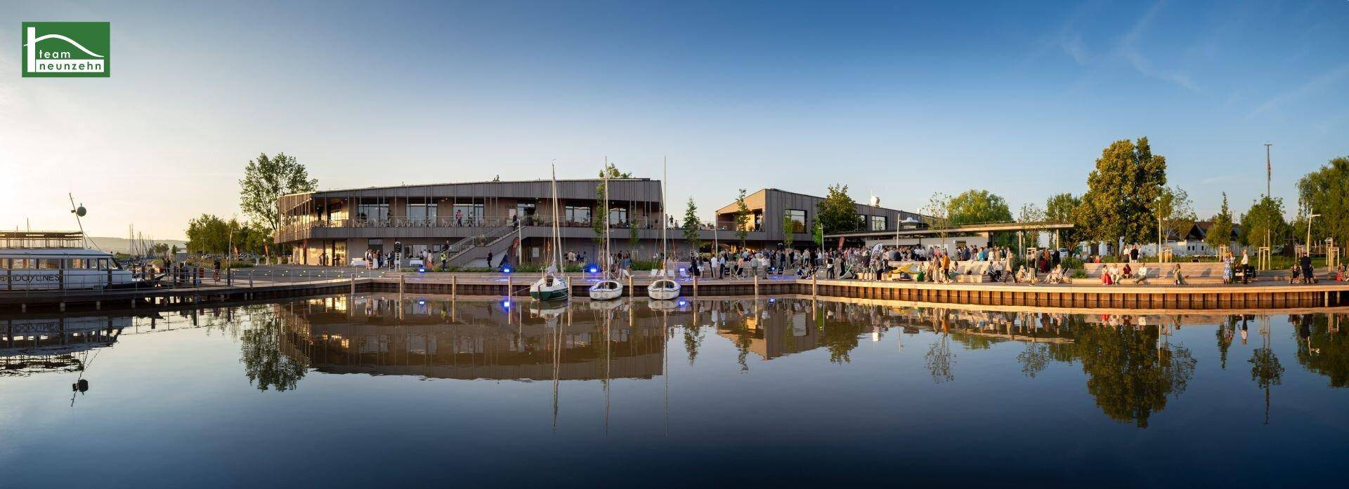 Moderne Gebäude am Ufer des Neusiedler Sees mit Bootsanlegestellen und Menschen.