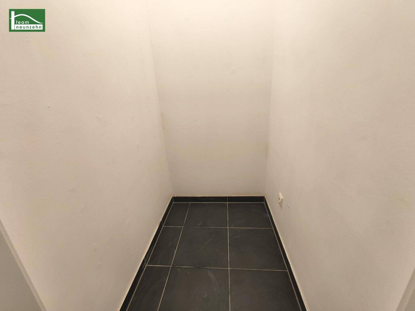 Praktischer Abstellraum mit dunklem Fliesenboden und weißen Wänden für zusätzlichen Stauraum.