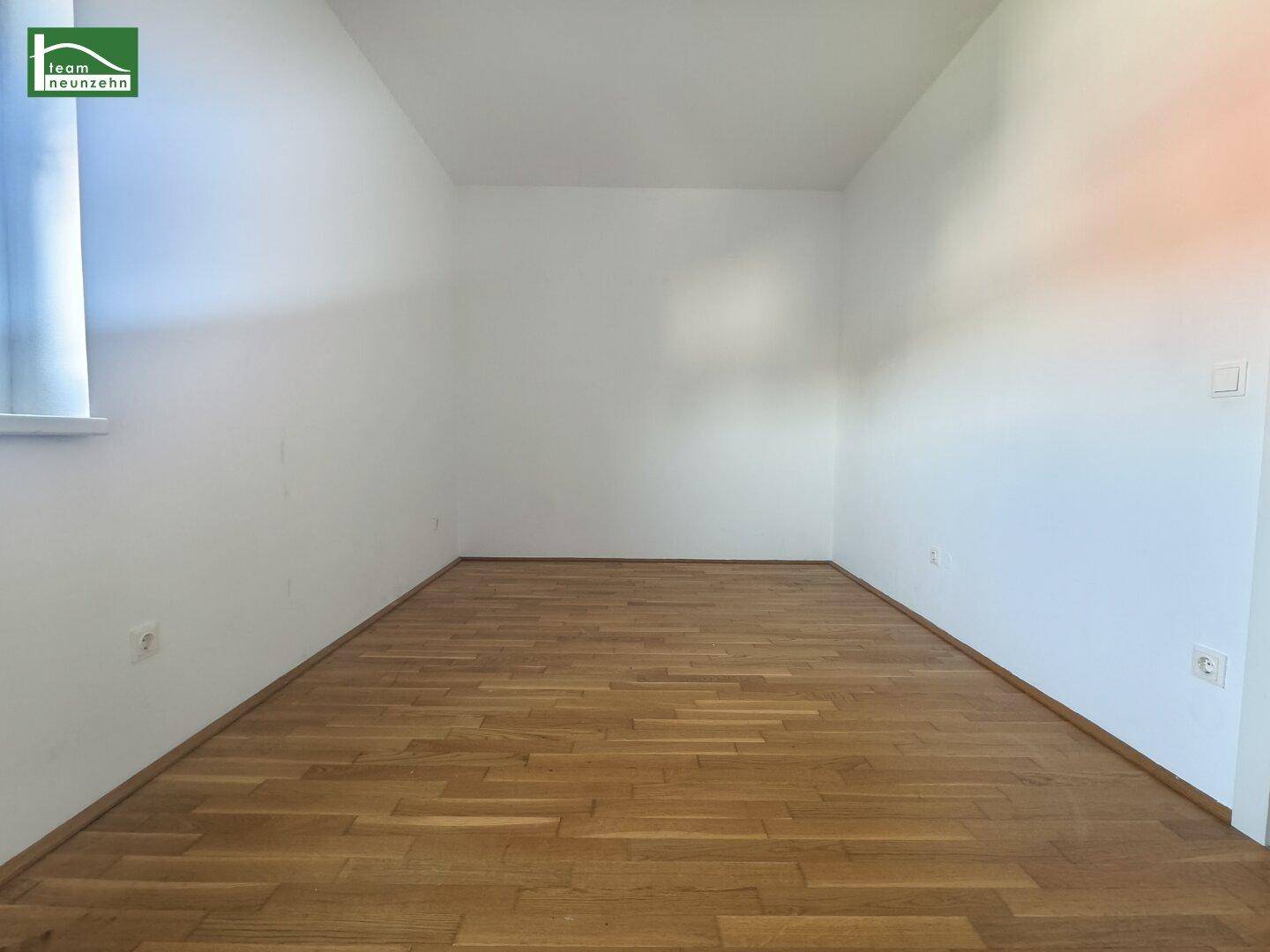 Lichtdurchflutetes Zimmer mit Parkettboden und weiß gestrichenen Wänden, ideal für verschiedene Zwecke.