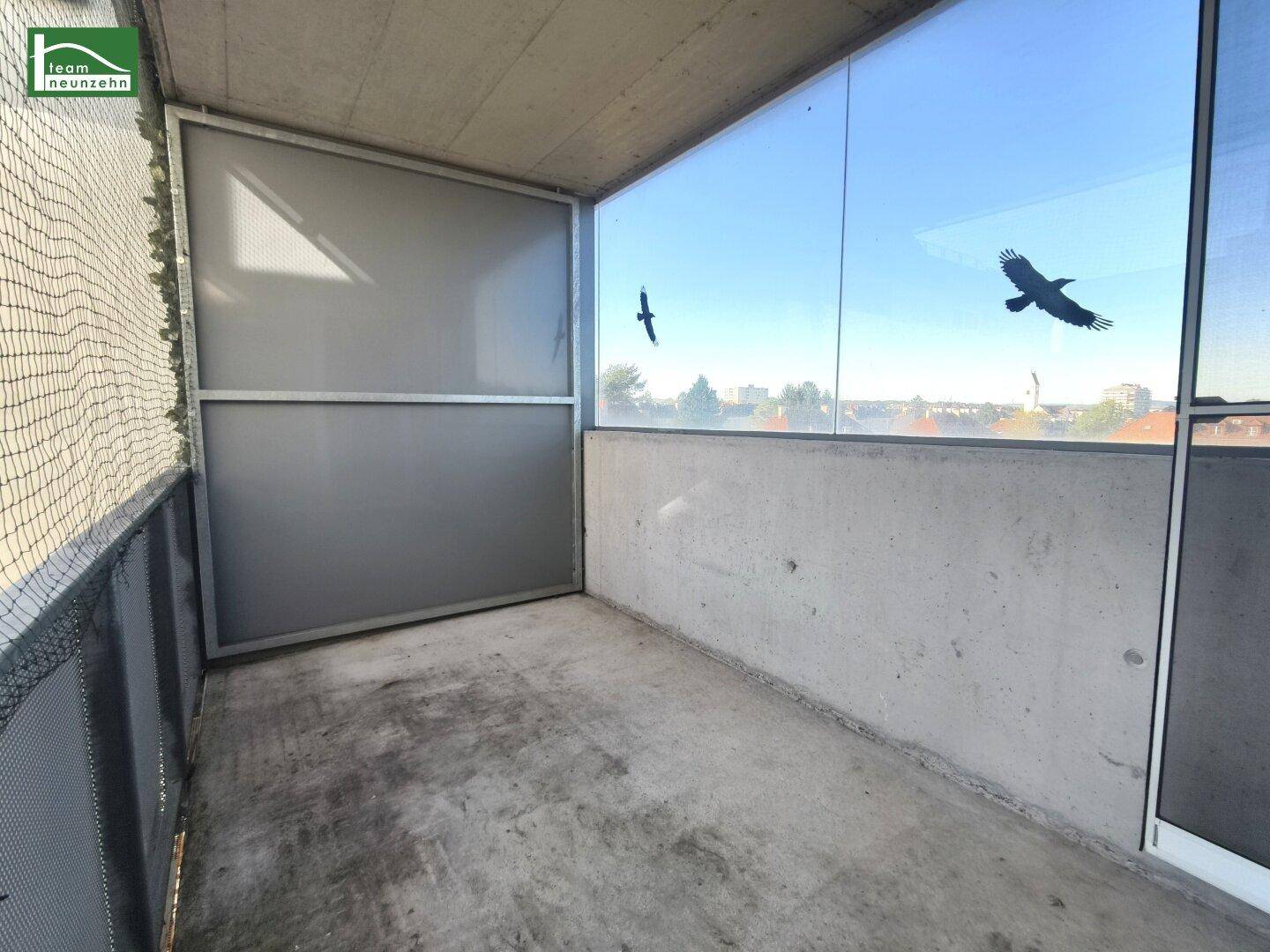 Verglaster Balkon mit Betonboden und weitem Blick über die Stadt.