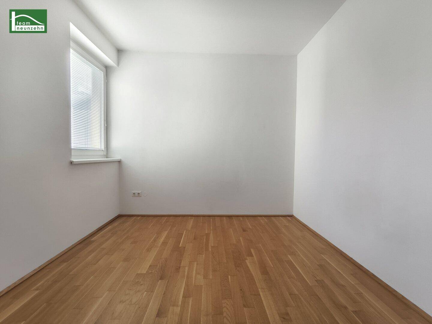 Helles Schlafzimmer mit Parkettboden und einem Fenster, bereit zur individuellen Gestaltung.