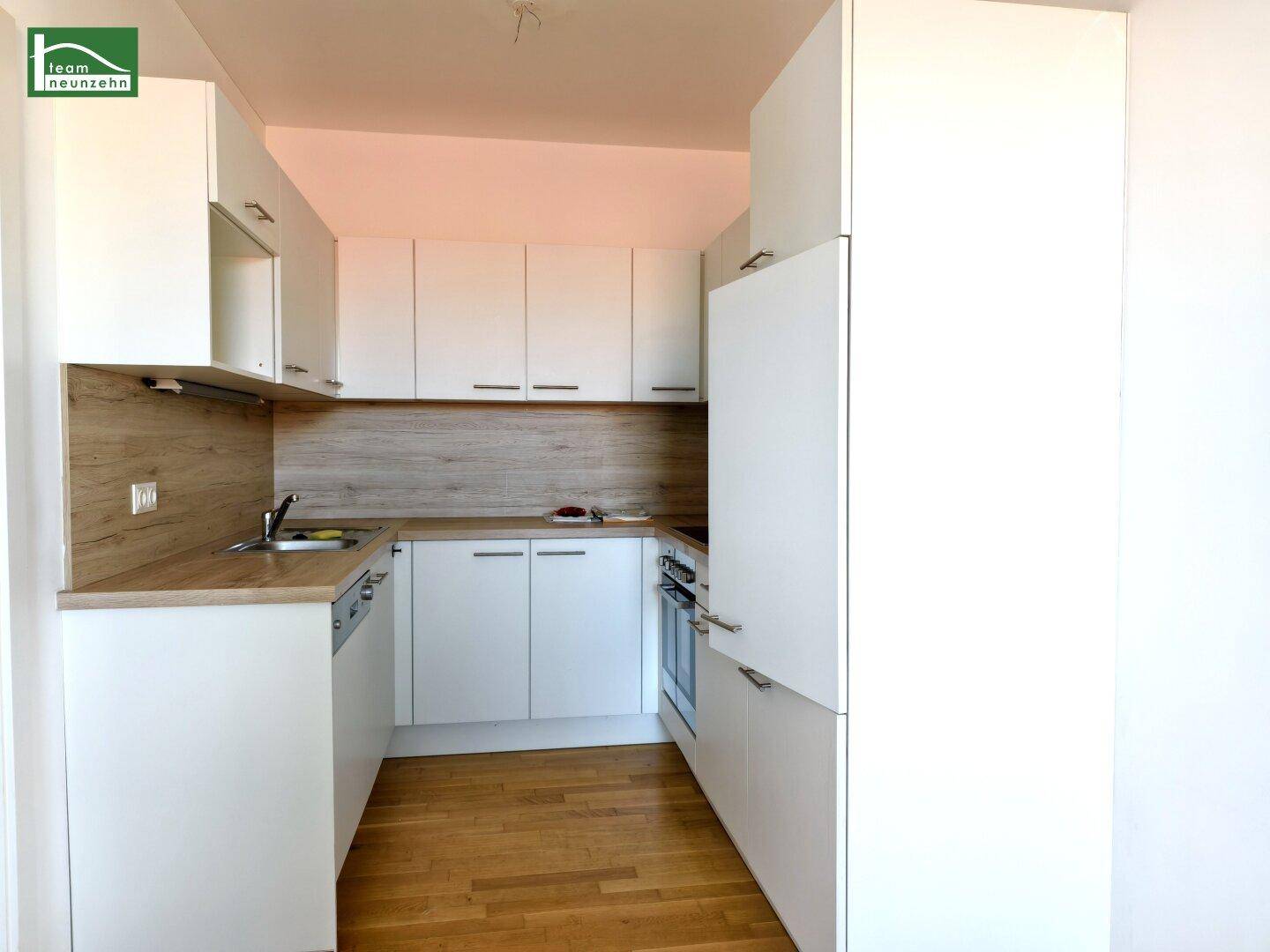 Moderne Einbauküche mit weißen Schränken, Holzoptik-Arbeitsplatte und integrierten Geräten.
