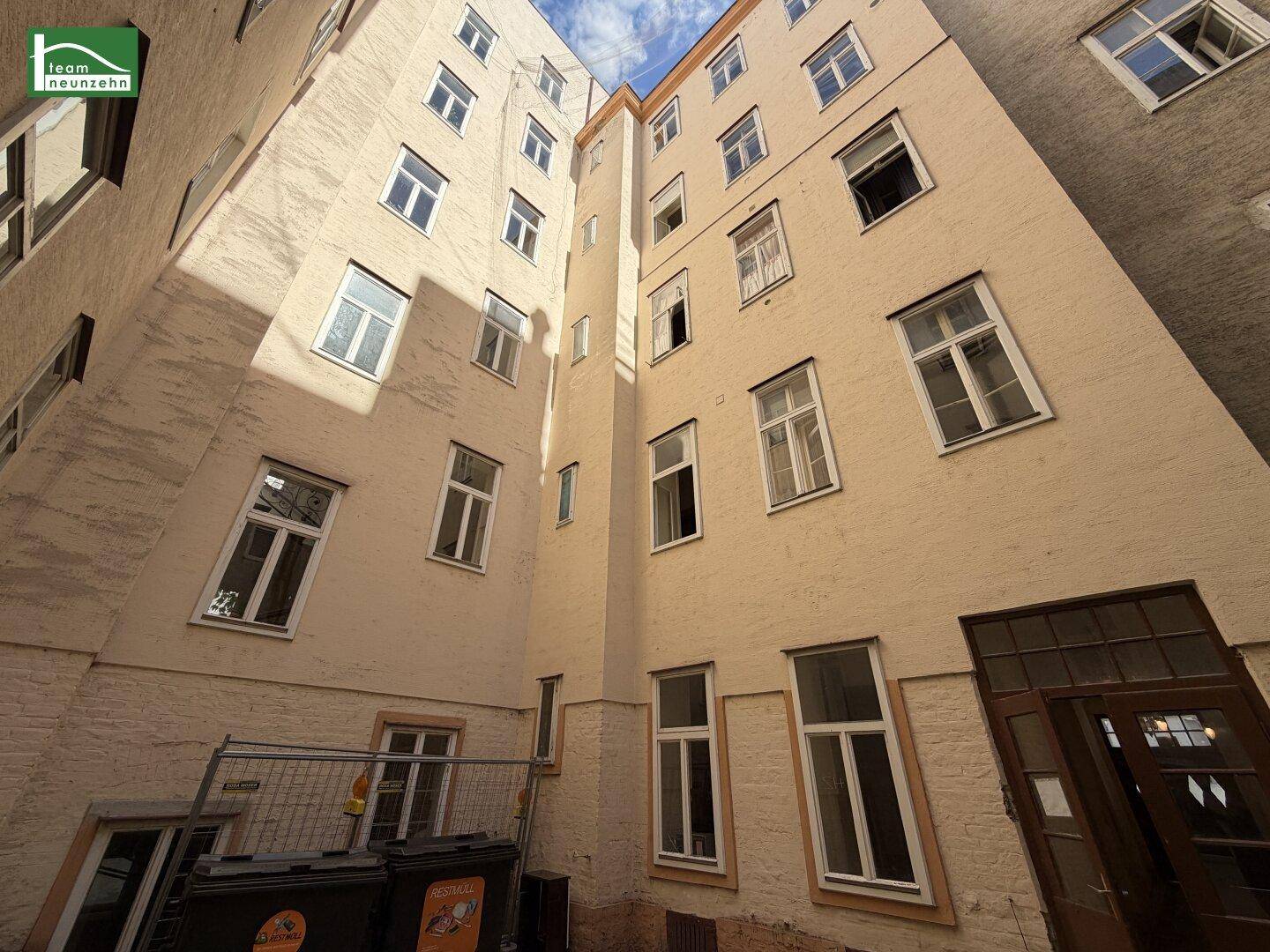 Innenhof eines Gebäudes mit vielen Fenstern und hellen Fassaden, von unten nach oben fotografiert.