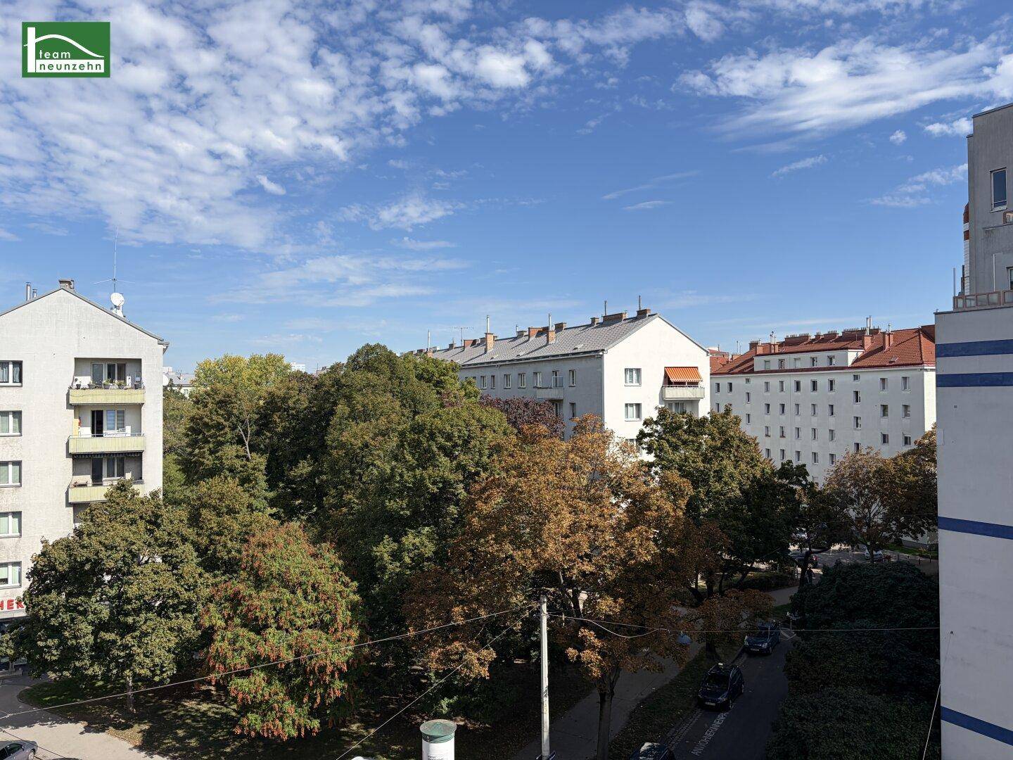 Weitläufiger Blick über die Stadt mit vielen Bäumen und Wohngebäuden unter blauem Himmel.