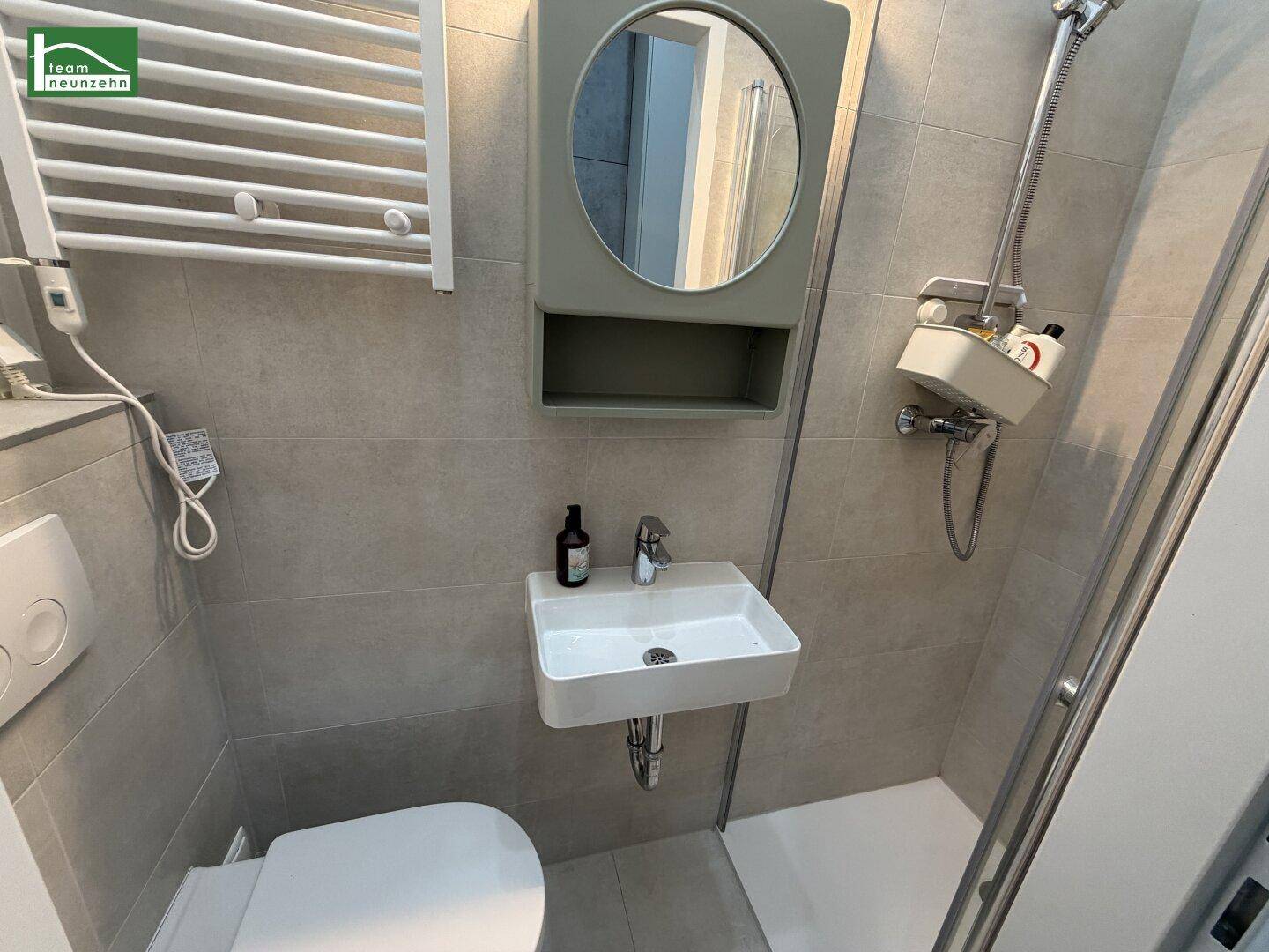 Modernes Badezimmer mit Dusche, WC, kleinem Waschbecken und beheiztem Handtuchhalter.