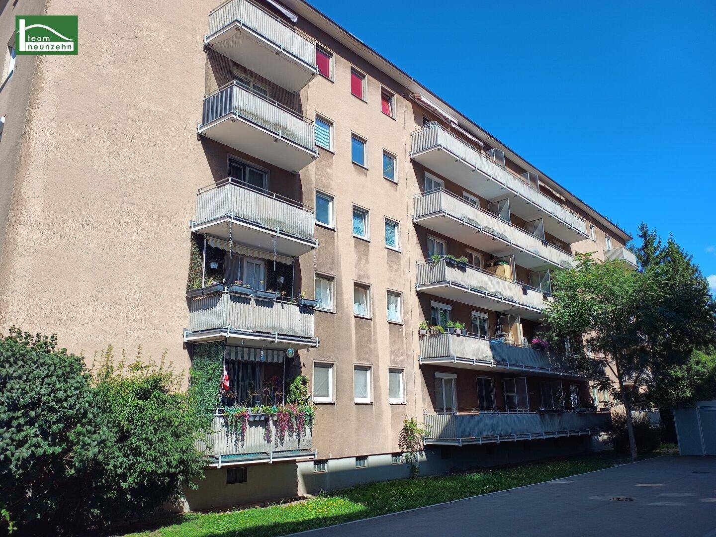 Detailansicht eines Mehrfamilienhauses mit vielen Balkonen und gepflegter Grünfläche.
