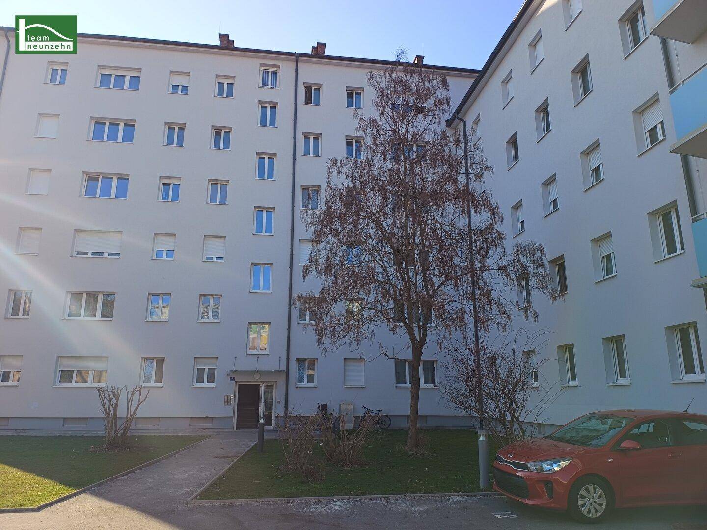 Wohngebäude mit heller Fassade, vielen Fenstern und einem Baum im Vordergrund.