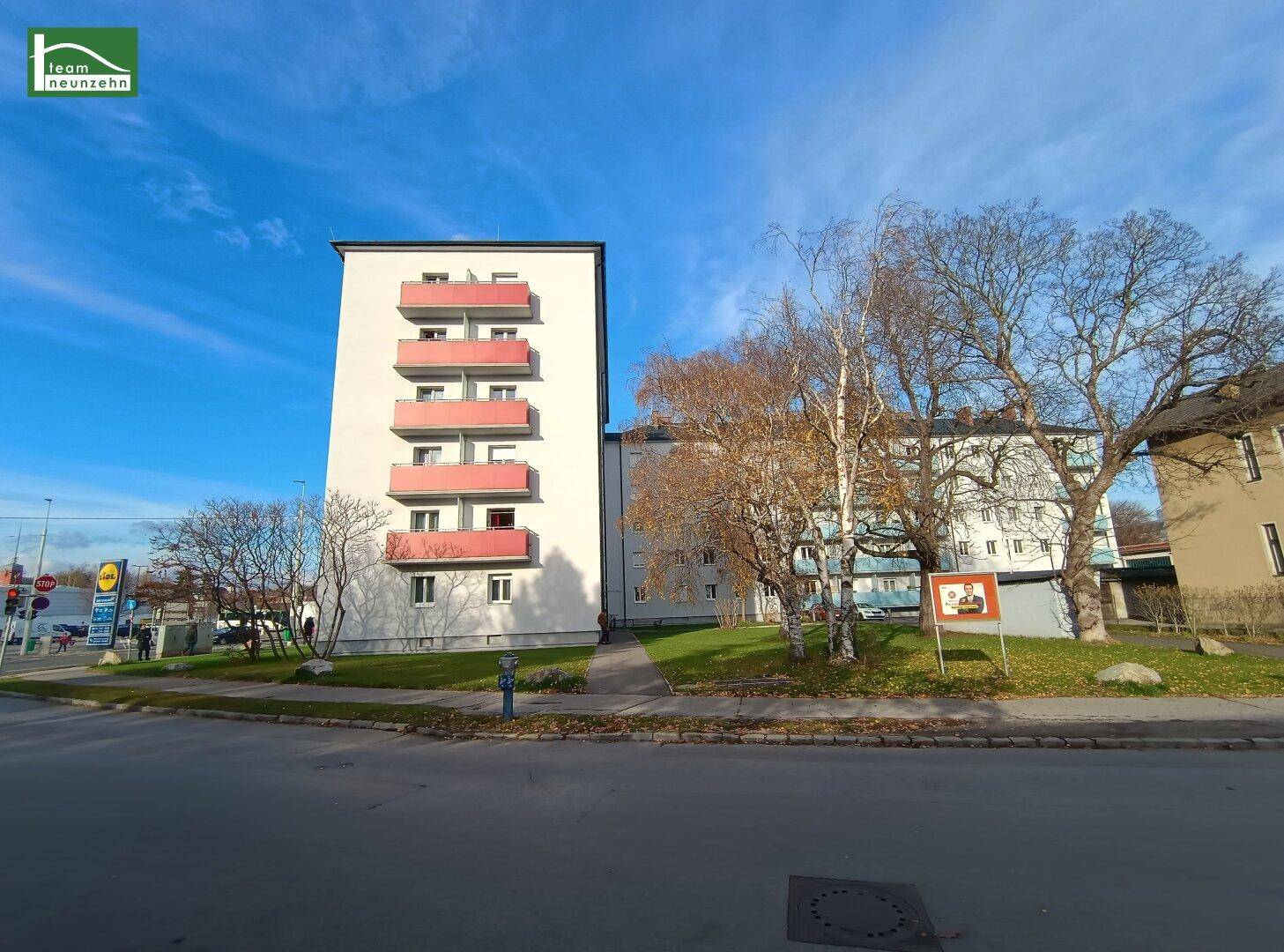 Mehrere Wohngebäude an einer Straße mit Bäumen und blauem Himmel.