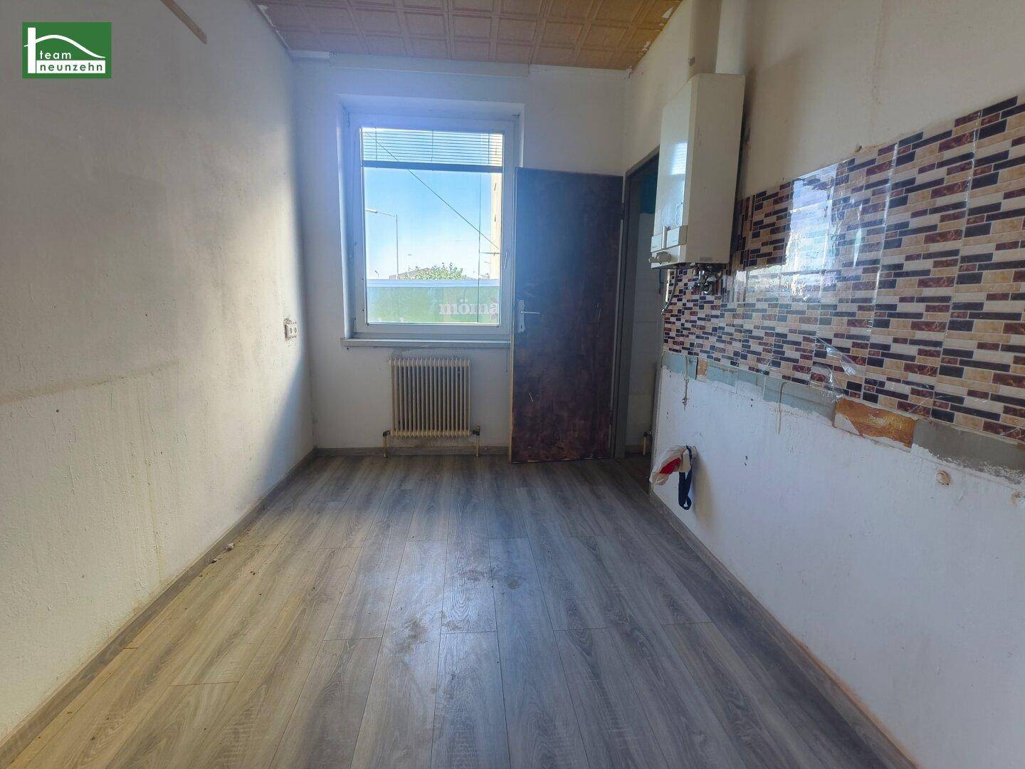 Leere Küche mit Fliesenrückwand, Laminatboden und Gastherme.