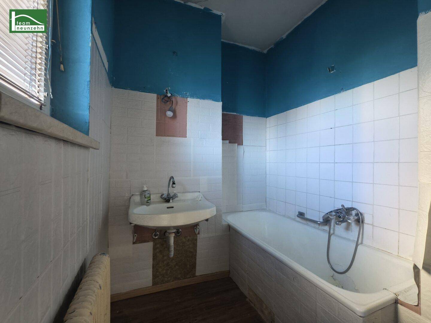 Badezimmer mit Badewanne, Waschbecken und blauen Wänden, renovierungsbedürftig.