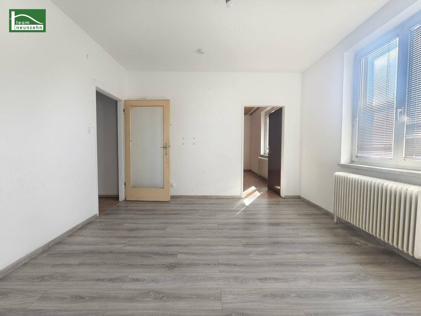 Geräumiges, leeres Zimmer mit Laminatboden und zwei Türöffnungen.