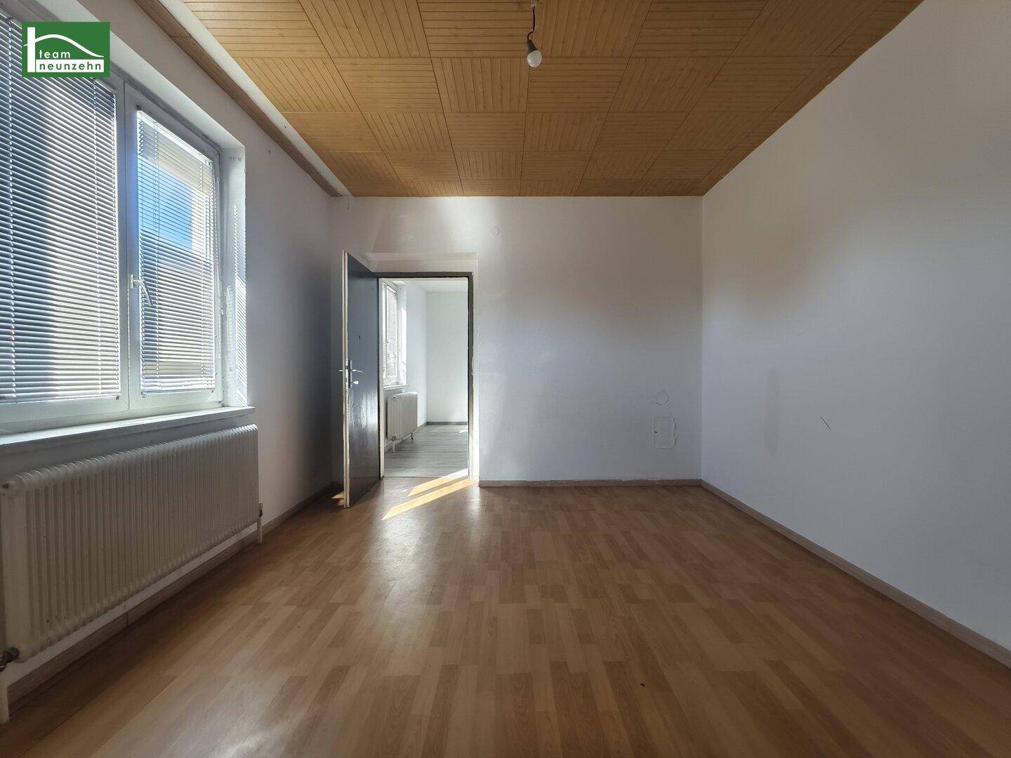 Helles Zimmer mit Parkettboden, Holzdecke und offener Tür zu einem weiteren Raum.