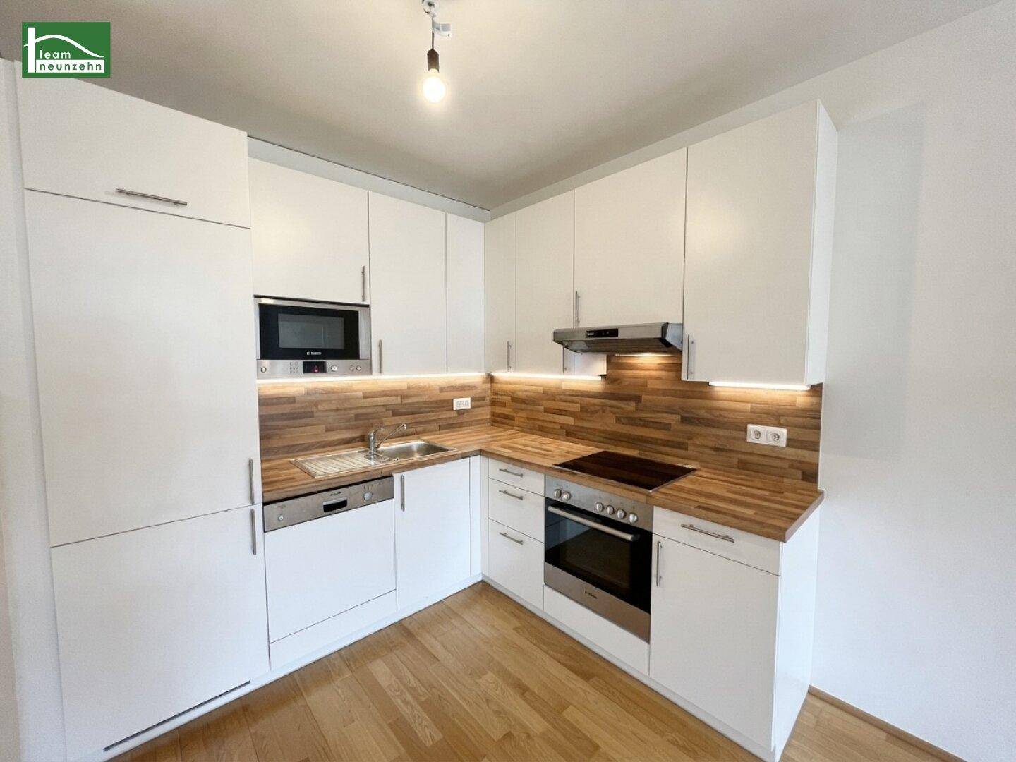 Moderne Einbauküche mit weißen Schränken, Holz-Arbeitsplatten und integrierten Geräten.