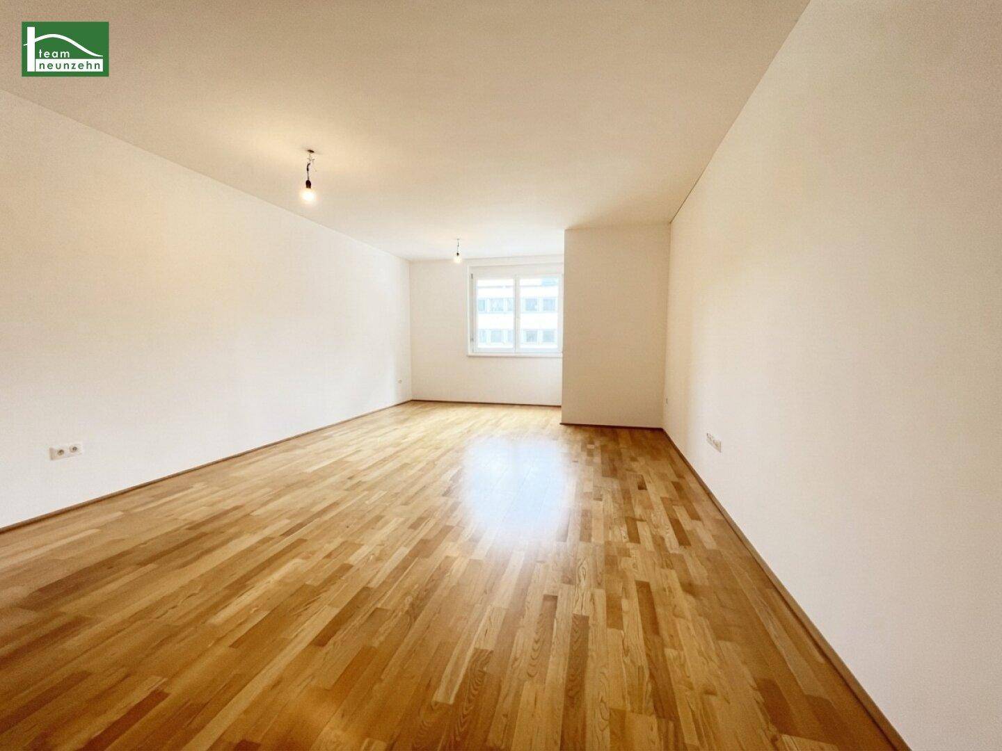 Geräumiger, heller Raum mit Parkettboden und weiß gestrichenen Wänden, ideal als Wohnzimmer.