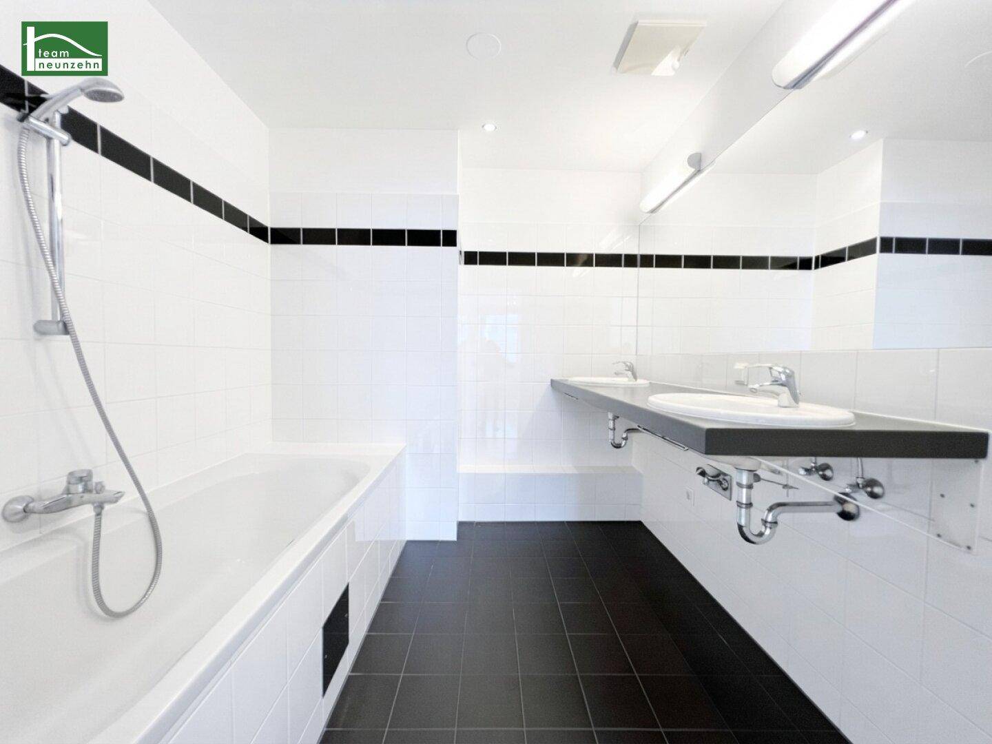 Modernes Badezimmer mit Badewanne, Dusche, Doppelwaschbecken und schwarz-weißen Fliesen.