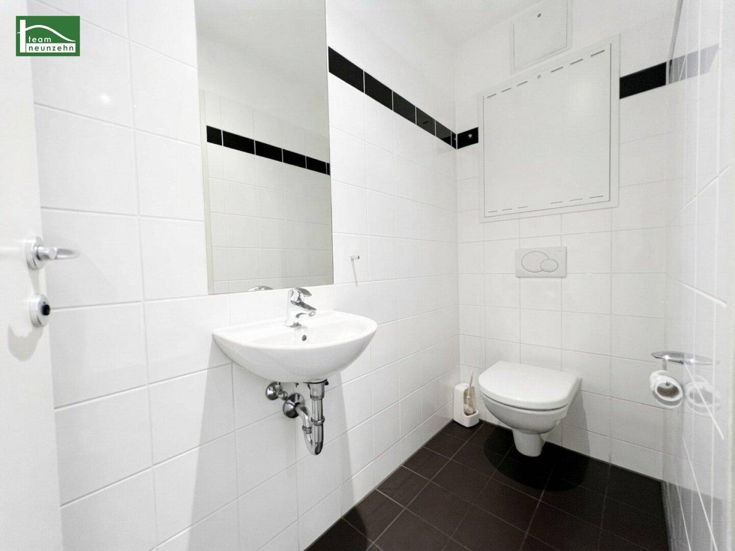 Separates WC mit wandhängender Toilette, kleinem Waschbecken und Spiegel.