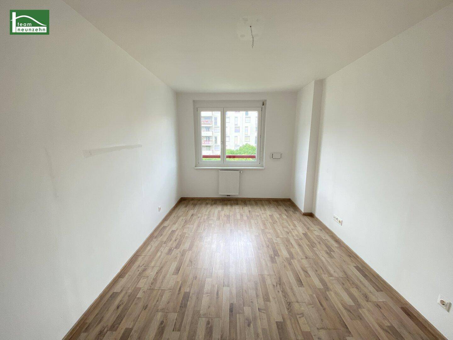 Leeres Schlafzimmer mit hellem Holzboden und einem Fenster mit Blick nach draußen.