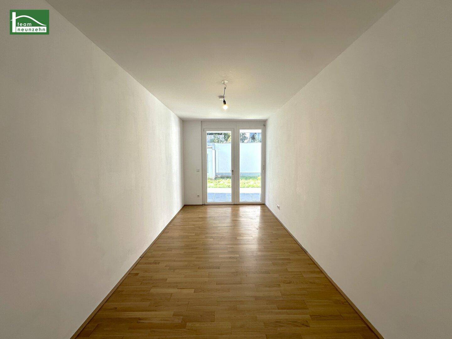 Heller, leerer Raum mit Parkettboden und Zugang zu einem Außenbereich.