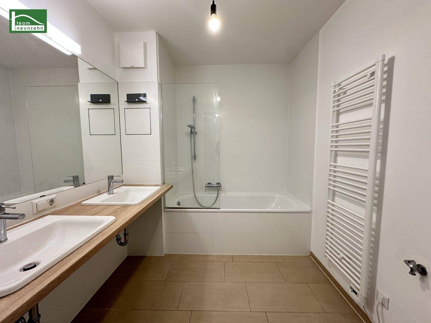 Modernes Badezimmer mit Doppelwaschbecken, Badewanne und beheiztem Handtuchhalter.