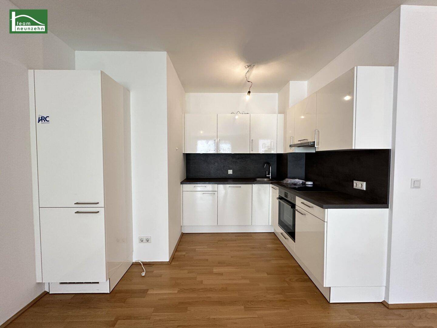 Moderne Einbauküche mit weißen Hochglanzfronten und dunkler Arbeitsplatte.