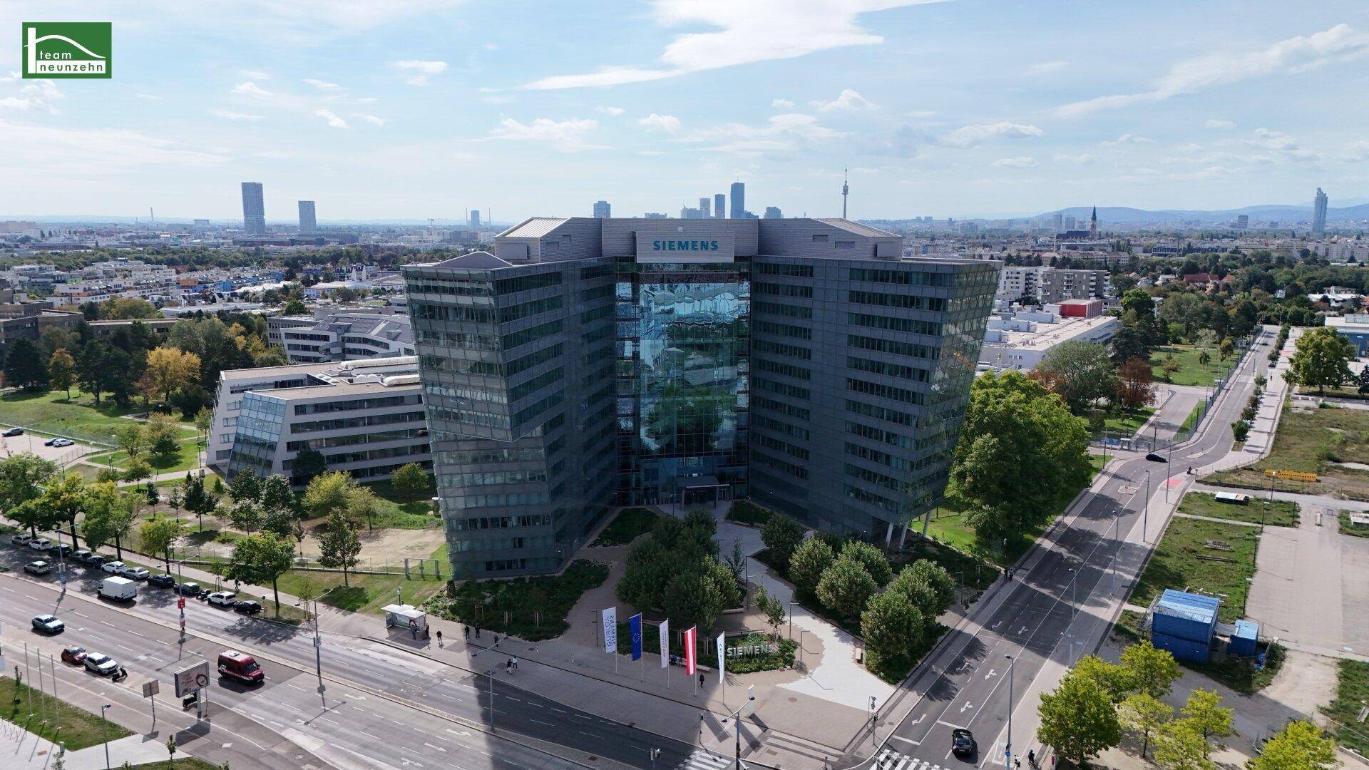 Luftaufnahme eines großen, modernen Bürogebäudes mit Glasfassade in städtischer Umgebung.
