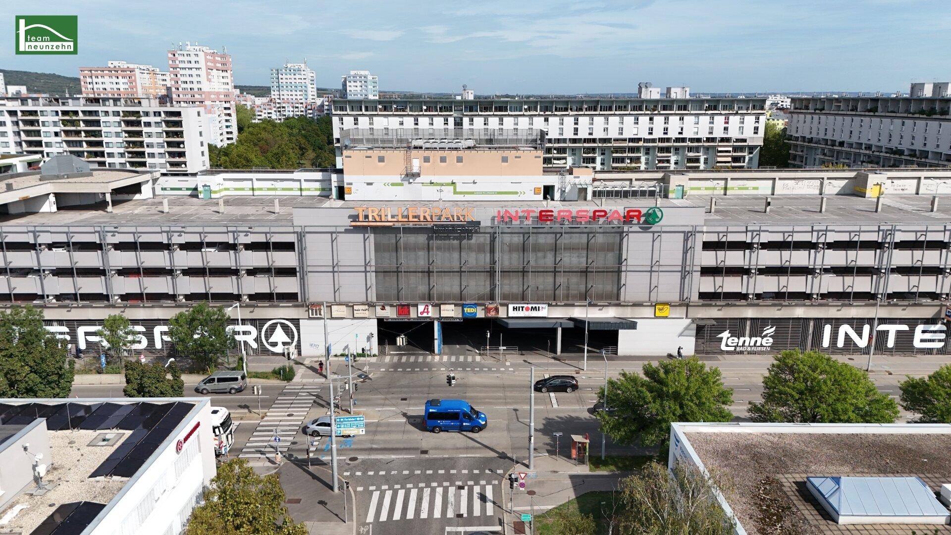 Luftaufnahme eines Einkaufszentrums mit Parkhaus und umliegenden Wohngebäuden.