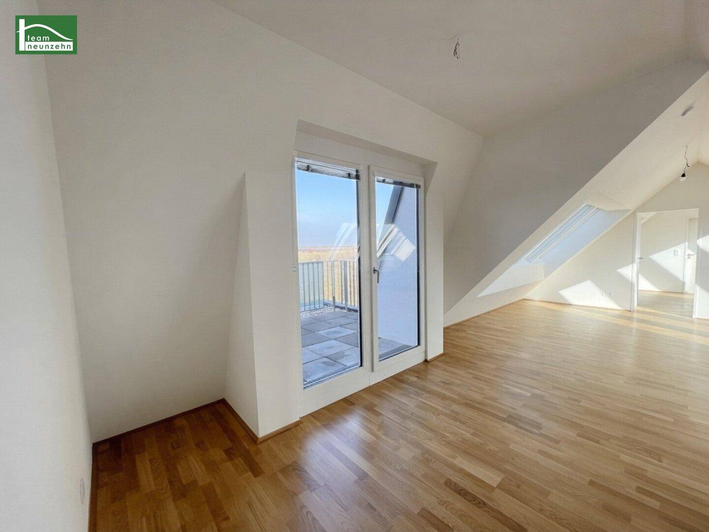 Geräumiges Wohnzimmer im Dachgeschoss mit Holzboden und Zugang zu einem kleinen Balkon.