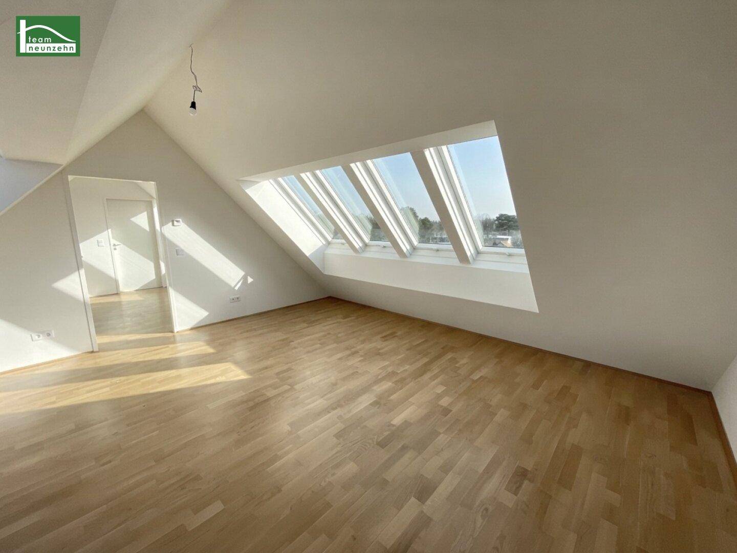 Helles, leeres Wohnzimmer im Dachgeschoss mit schrägen Wänden und großen Dachfenstern.