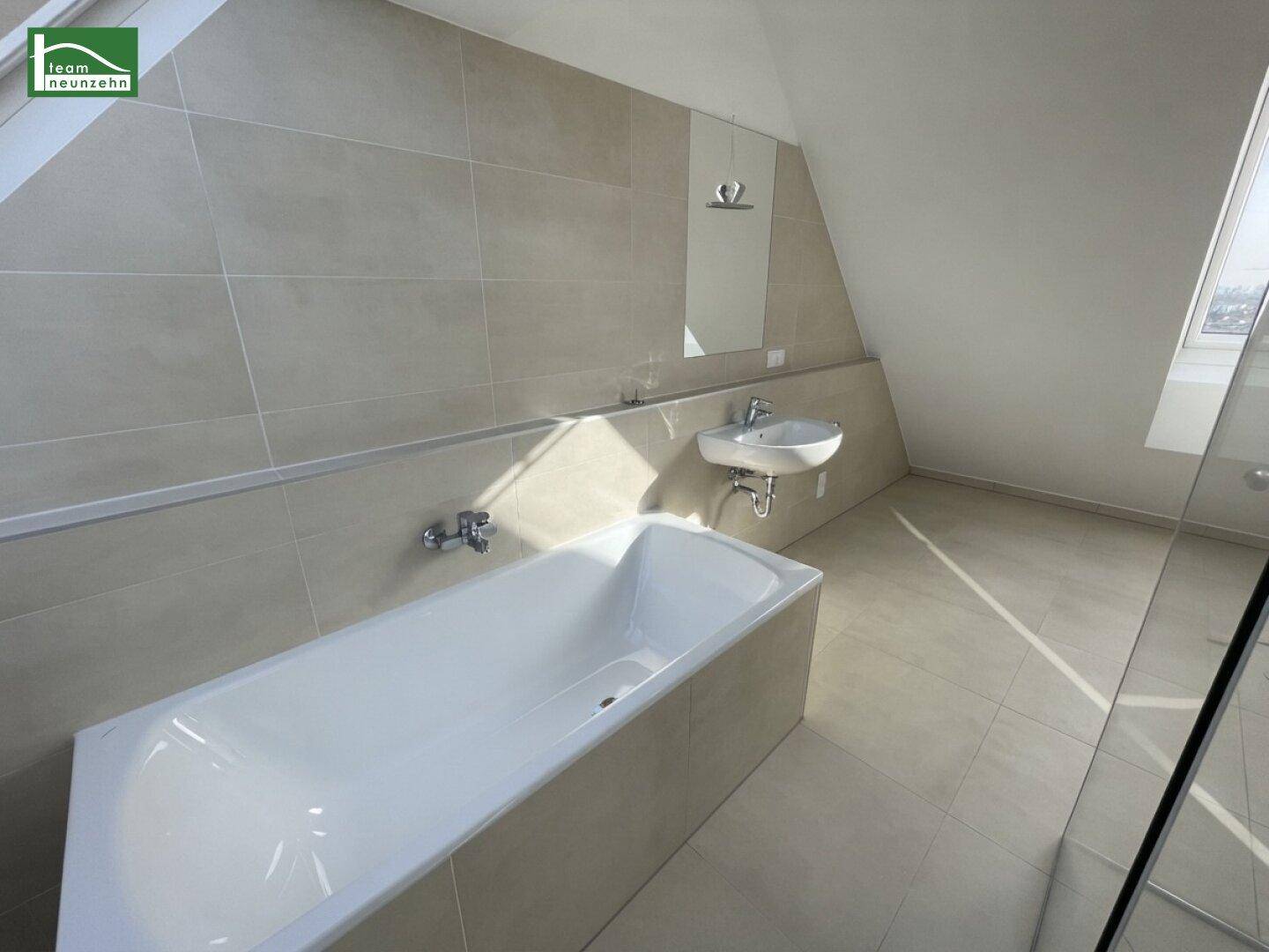 Helles Badezimmer mit Badewanne, Fliesenboden und schrägen Wänden im Dachgeschoss.