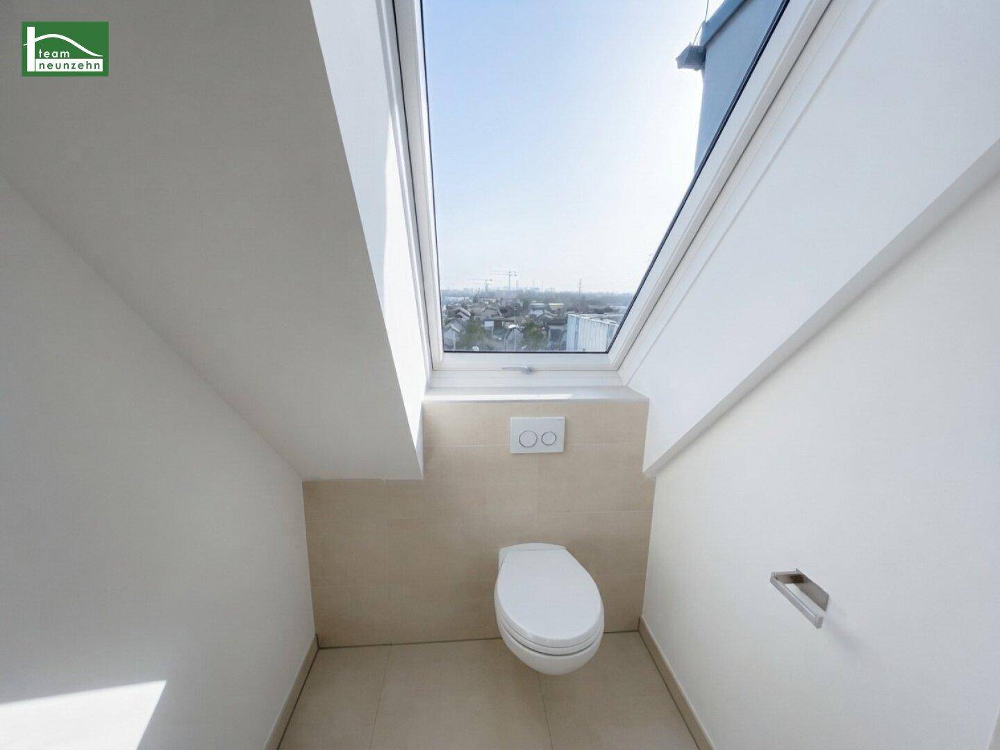 Separates WC mit wandhängender Toilette, Fliesen und Dachfenster für Belüftung.
