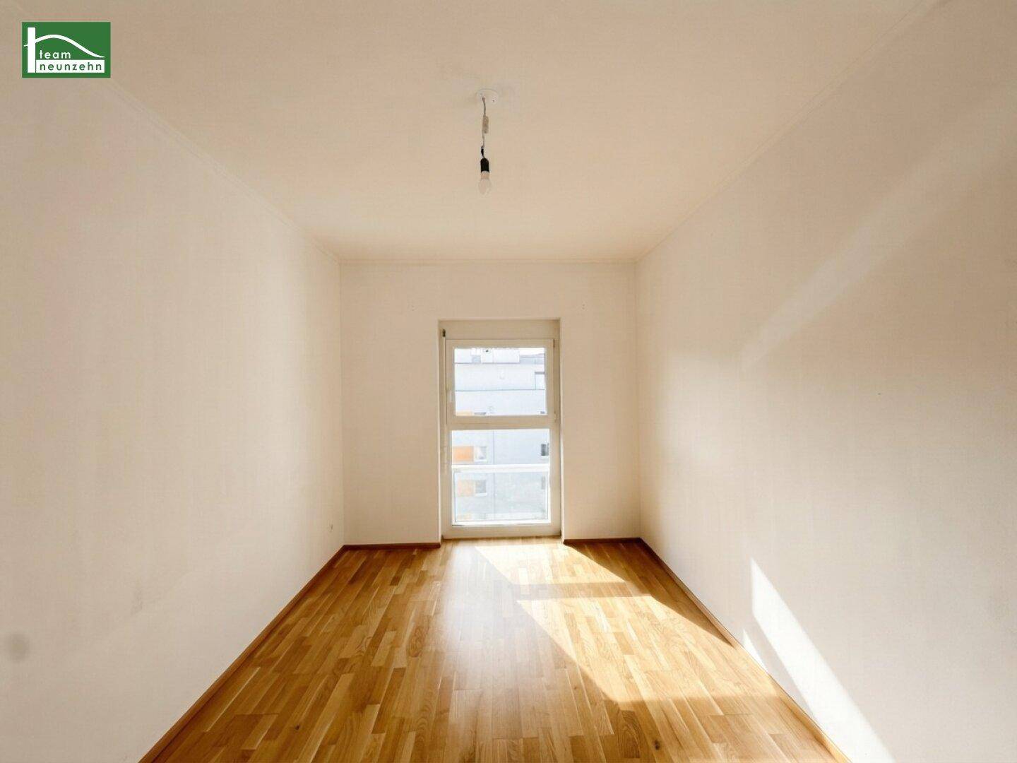 Helles Zimmer mit Parkettboden und einem Fenster, das viel Tageslicht hereinlässt.