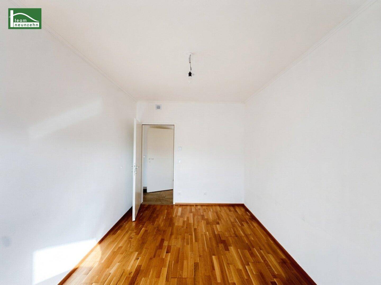 Leeres Zimmer mit Parkettboden und einer Tür, die zu einem weiteren Raum führt.