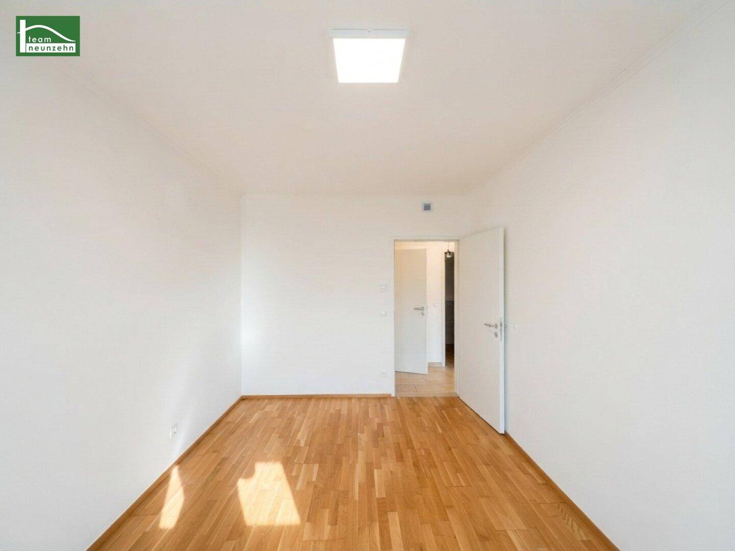 Schlichtes Zimmer mit Parkettboden und einer Tür, die den Zugang zu anderen Bereichen ermöglicht.