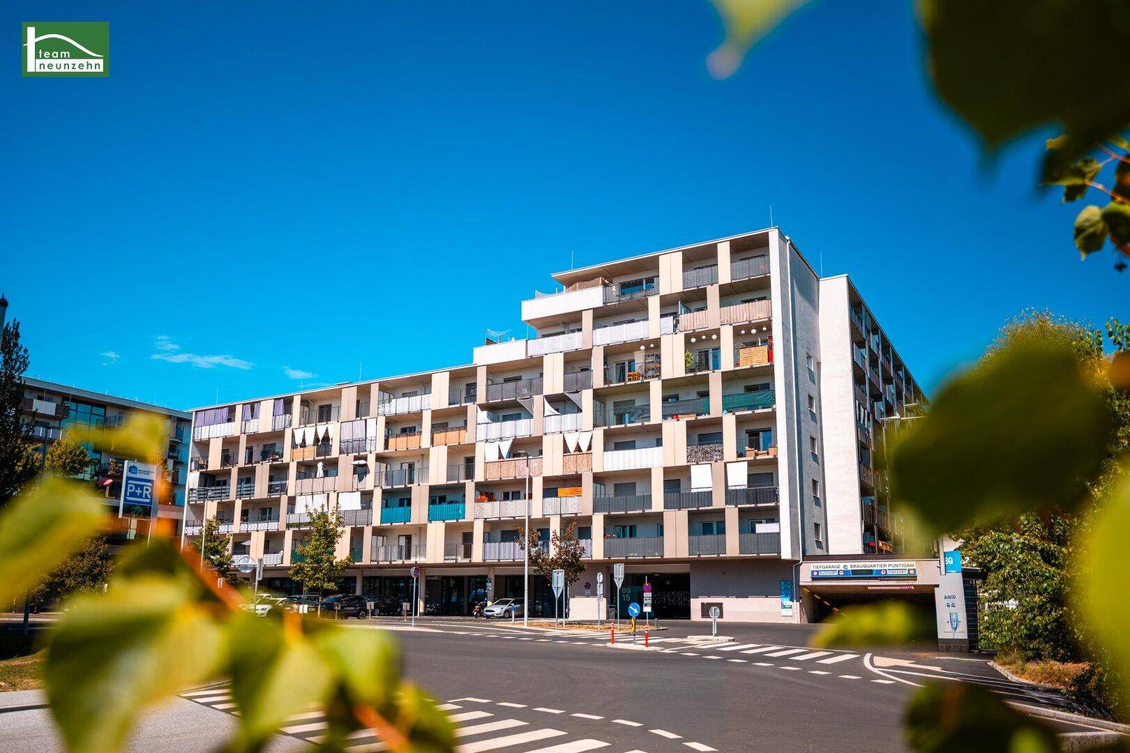 Modernes Mehrfamilienhaus mit zahlreichen Balkonen unter strahlend blauem Himmel.