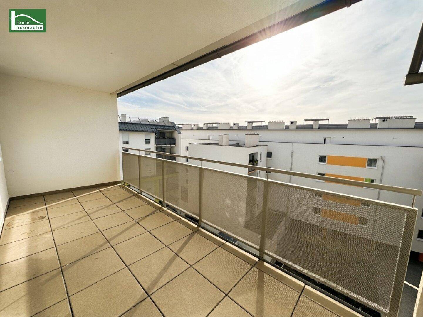 Sonniger Balkon mit Fliesenboden und modernem Geländer, bietet Blick auf die umliegenden Gebäude.