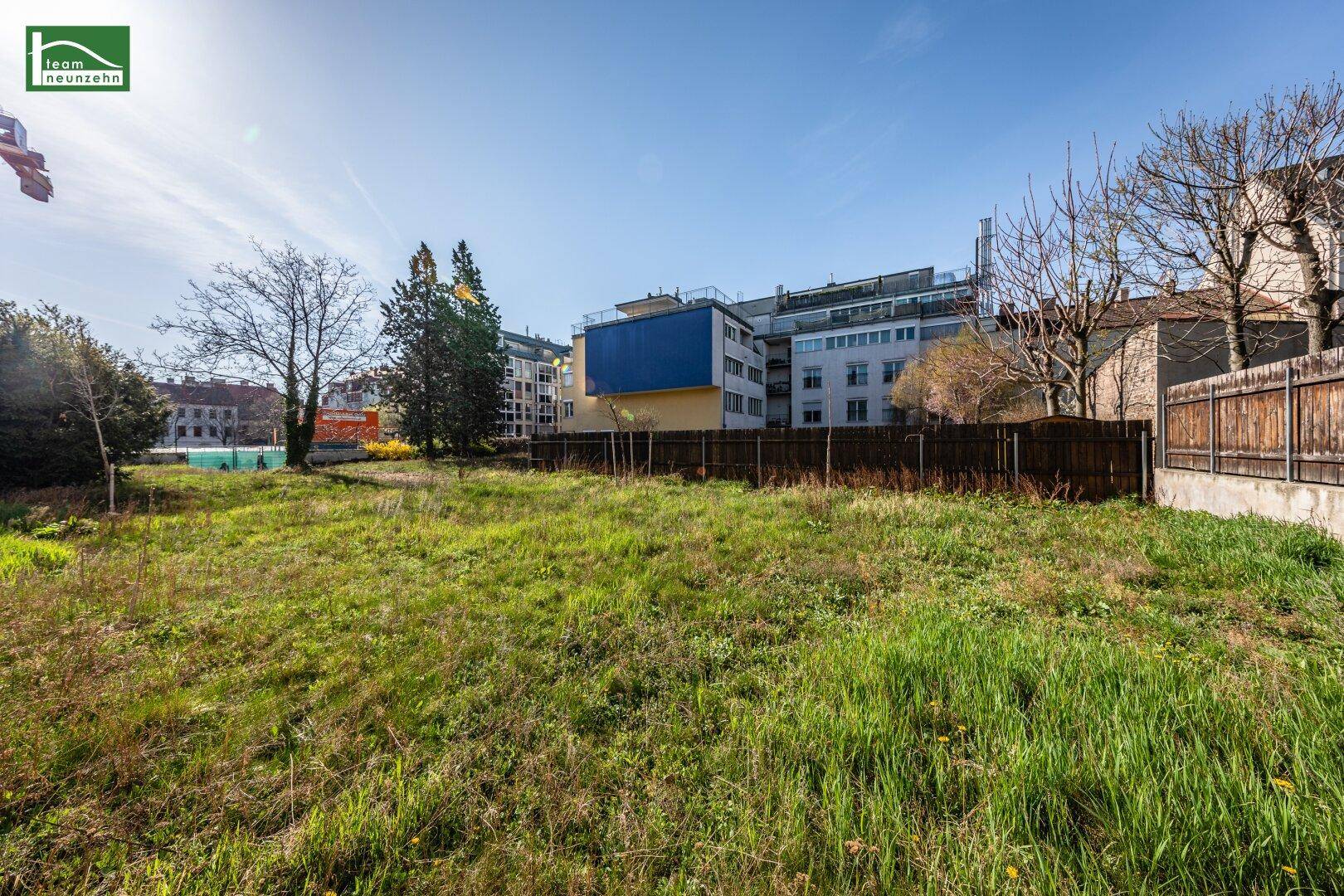 Sonniges, grünes Grundstück mit Blick auf moderne und ältere Gebäude in der Umgebung.