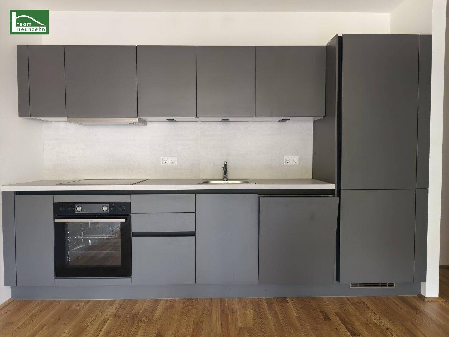 Moderne graue Küchenzeile mit integriertem Backofen, Kochfeld und Spüle.
