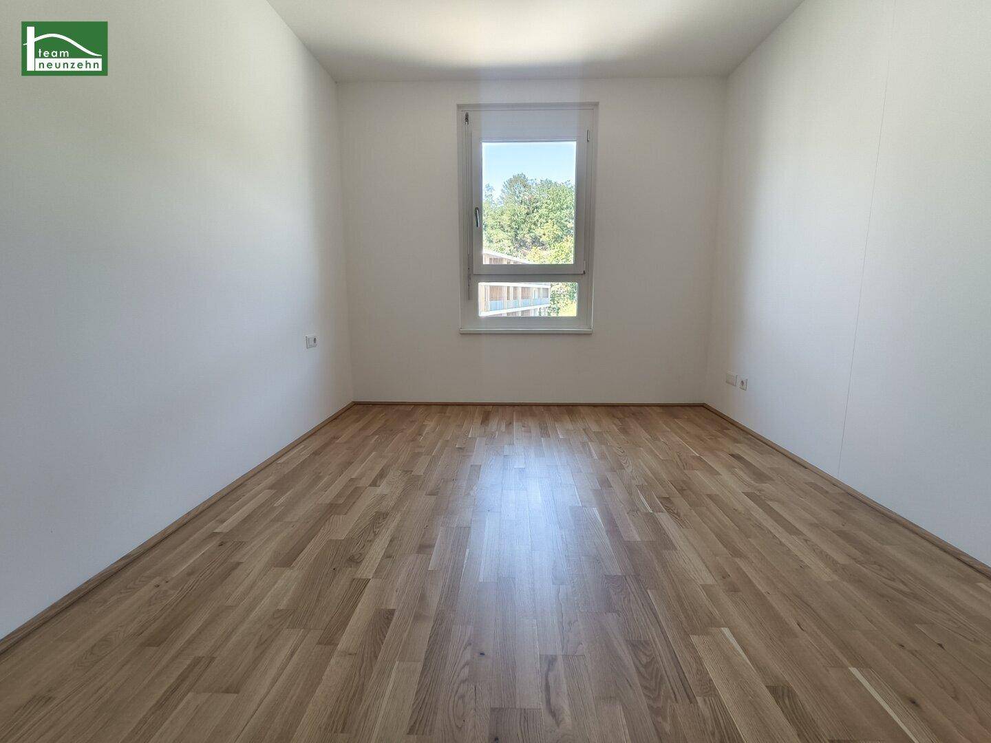 Helles Zimmer mit Holzboden und einem Fenster, das einen grünen Ausblick bietet.