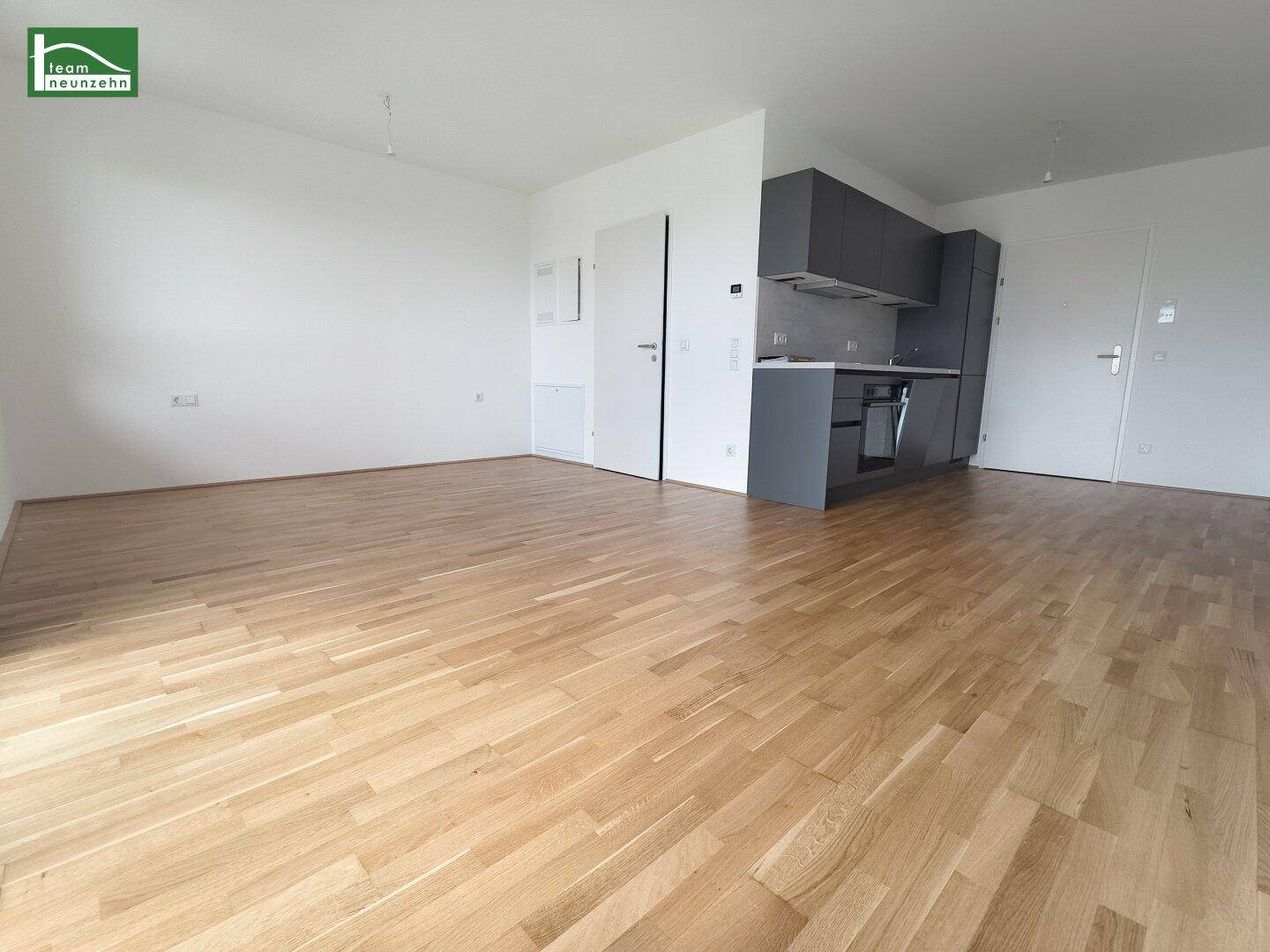Geräumiger Wohnbereich mit hellem Eichenparkett und moderner grauer Küchenzeile.