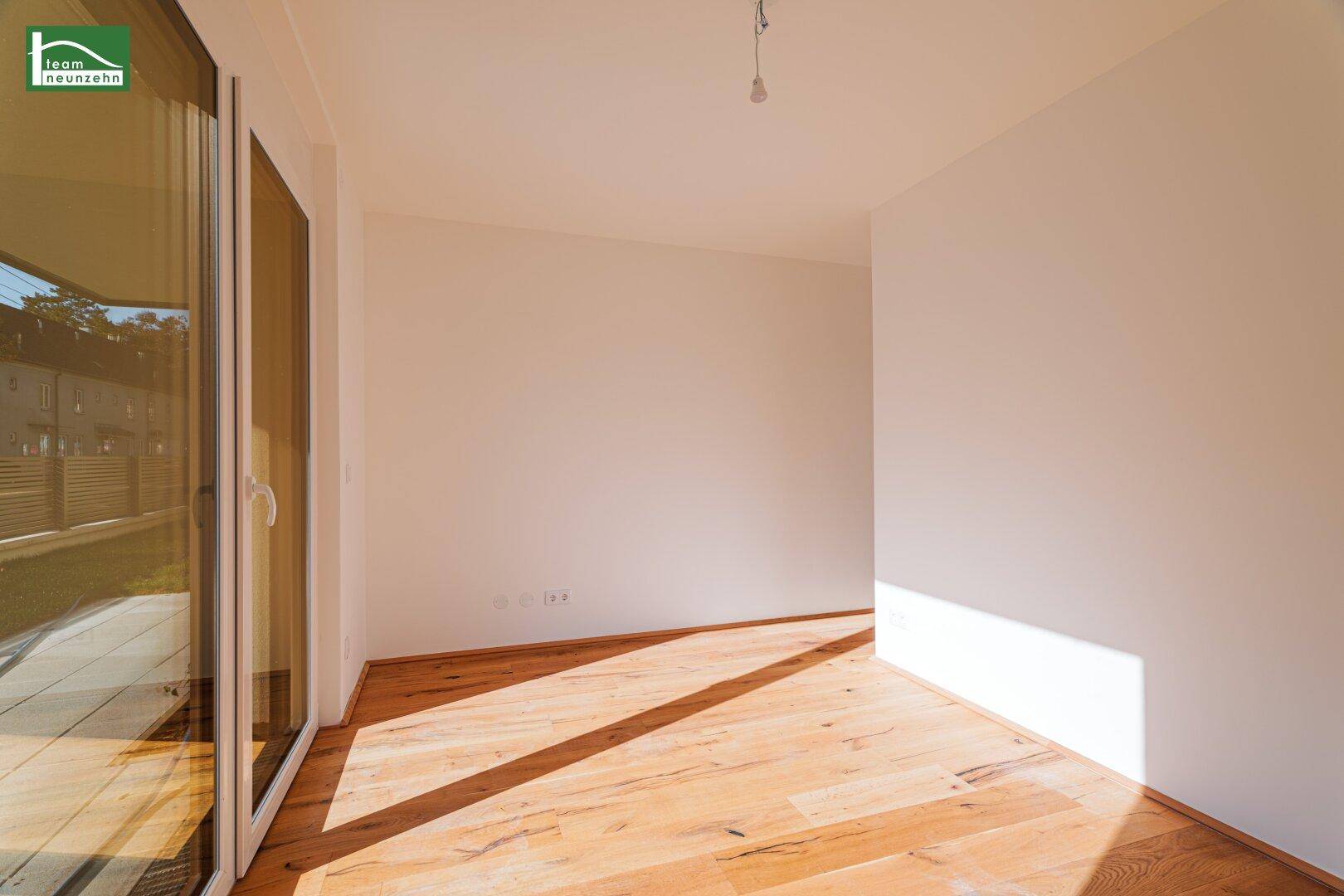 Heller Raum mit Holzdielenboden und großem Fenster, das viel Sonnenlicht hereinlässt.