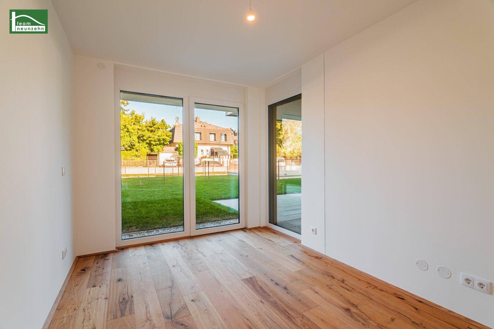 Geräumiges Zimmer mit Holzboden und großen Fenstern, die viel Tageslicht hereinlassen.
