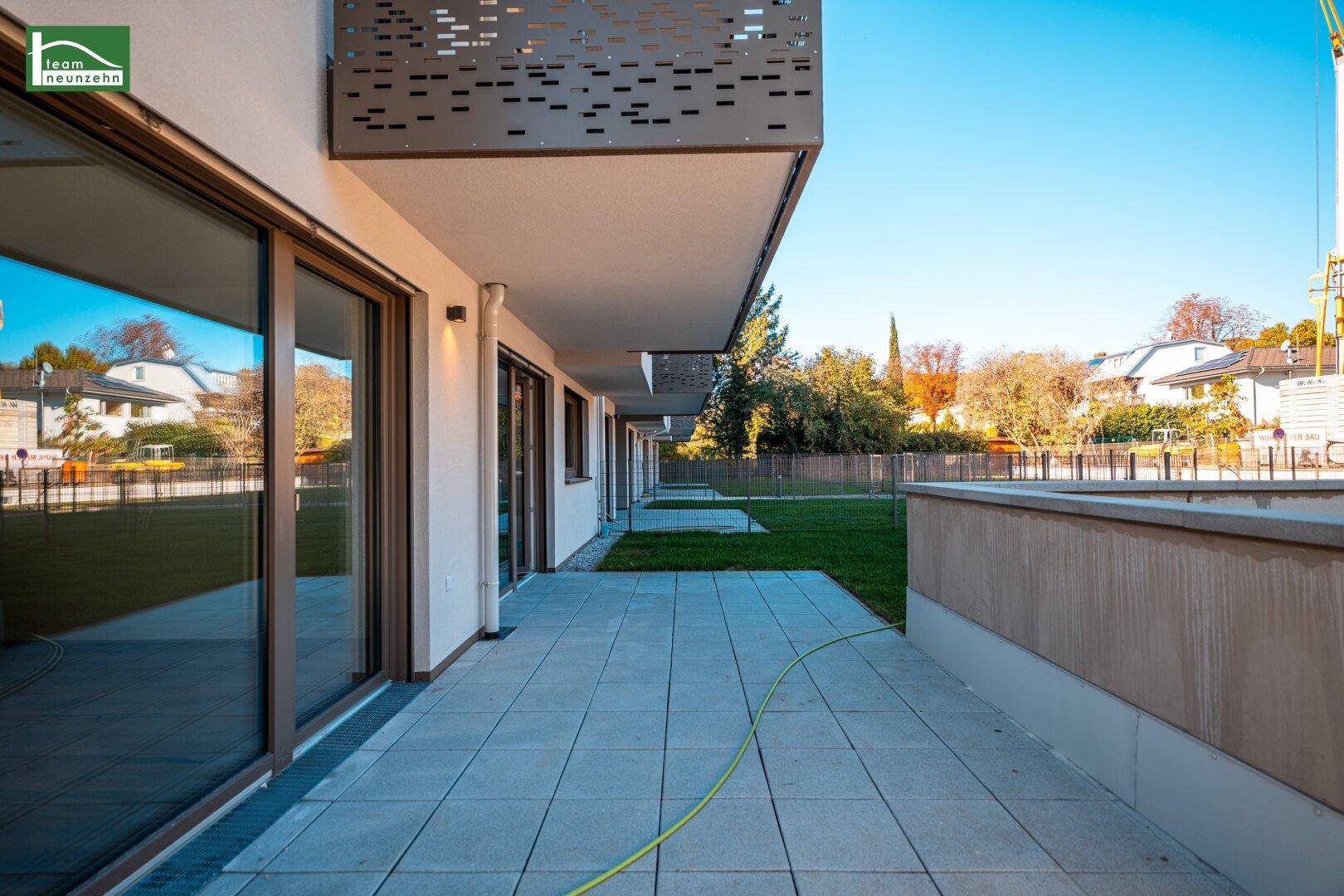 Lange, gepflasterte Terrasse entlang des Gebäudes mit Blick auf den Garten und die Umgebung.