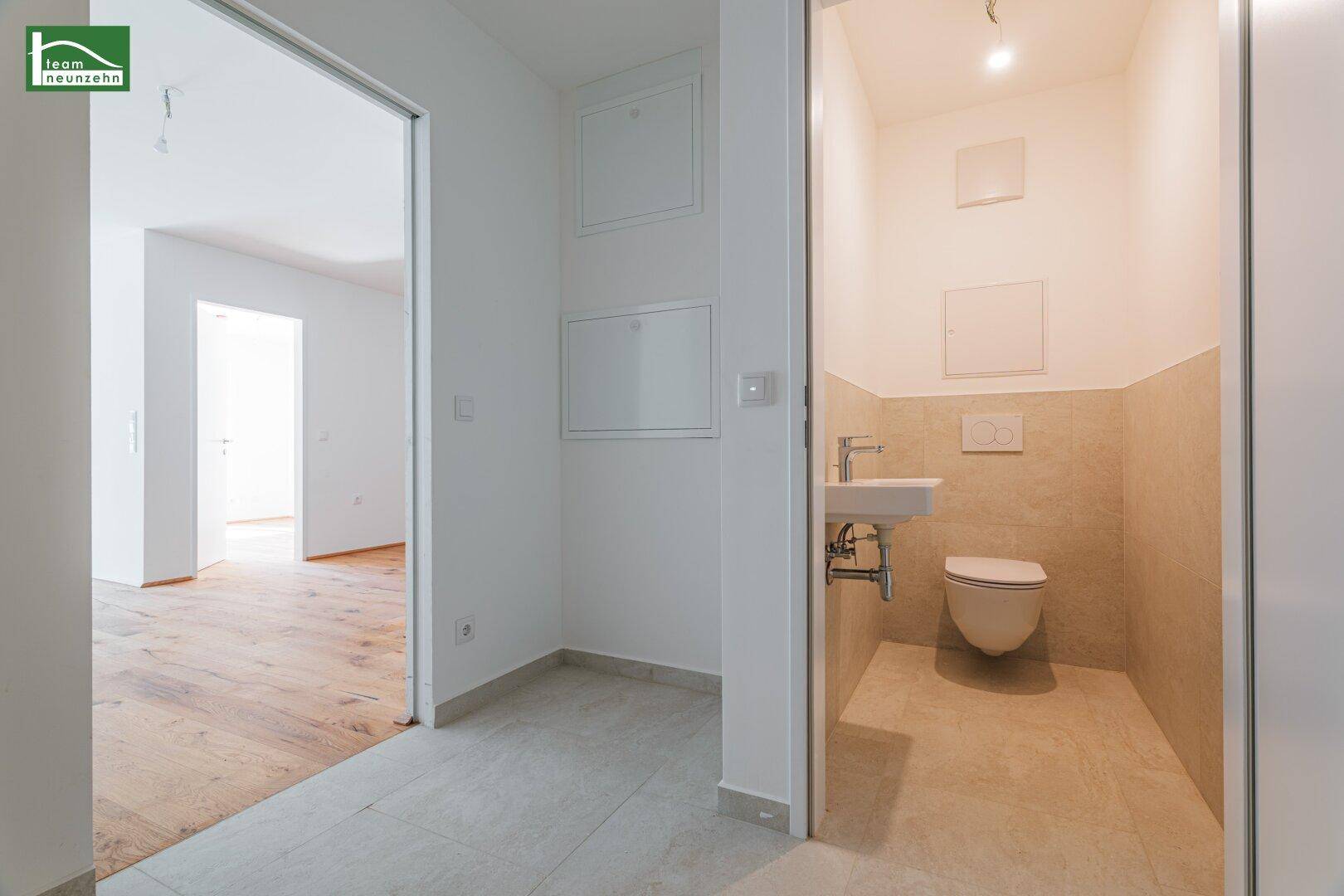 Kompaktes Gäste-WC mit Wand-WC, kleinem Waschbecken und hellen Fliesen.