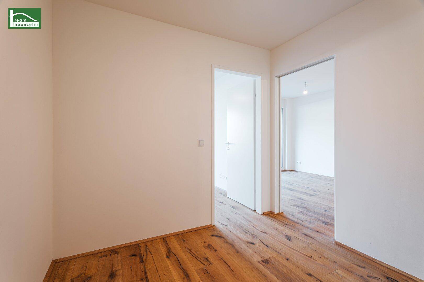 Schlichter Flur mit Holzboden und weißen Wänden, der verschiedene Wohnbereiche miteinander verbindet.