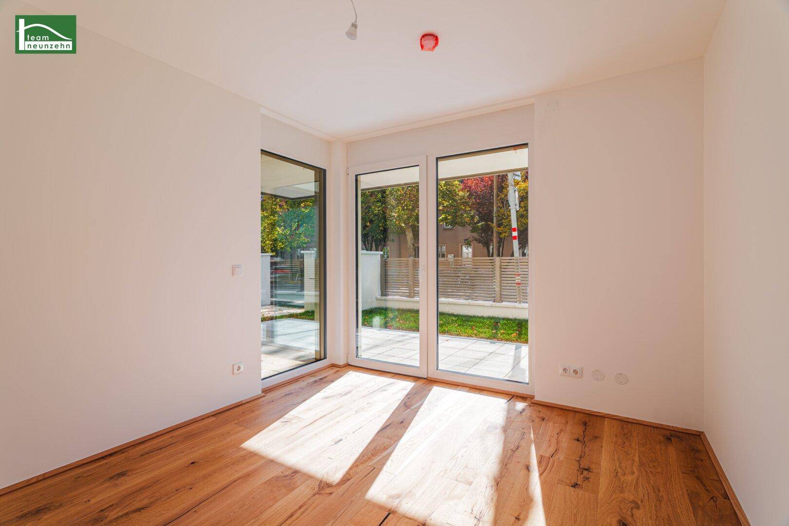 Helles Zimmer mit Holzboden und großen Fenstern, die viel Tageslicht hereinlassen.