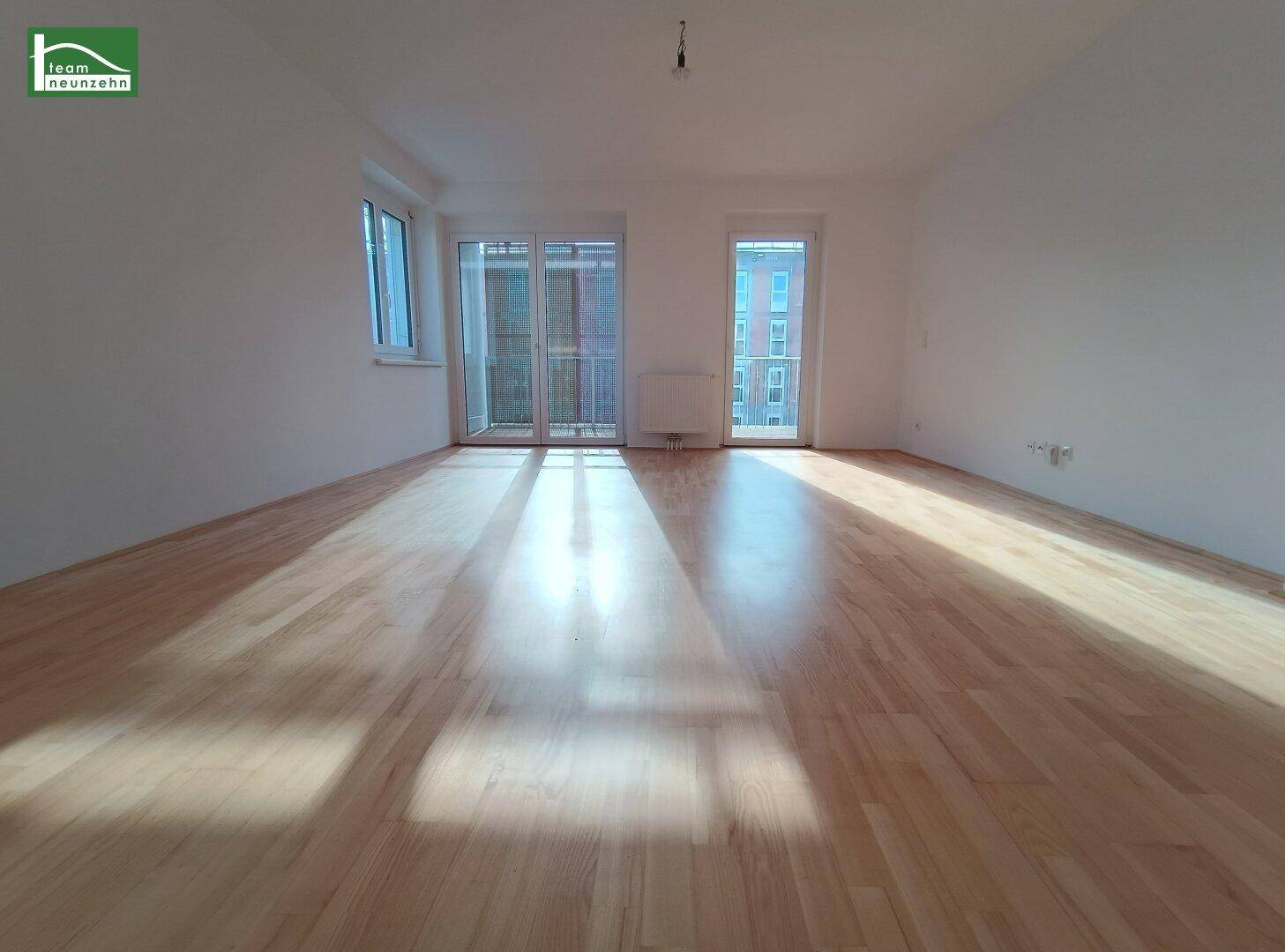 Helles, leeres Zimmer mit hellem Holzparkett und Zugang zu einem Balkon, durchflutet von natürlichem Licht.
