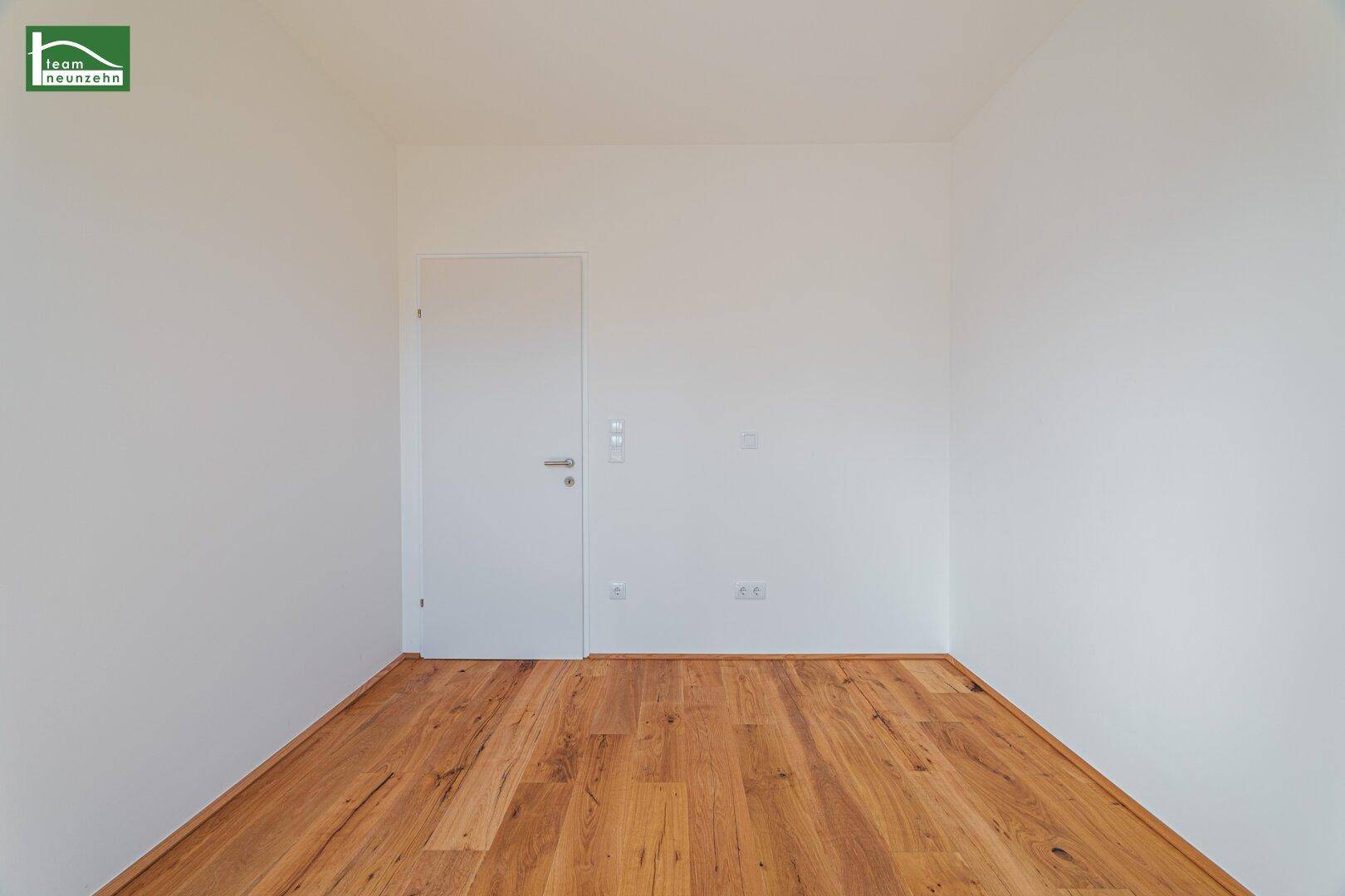 Schlichtes, leeres Zimmer mit Holzboden und weiß gestrichenen Wänden.